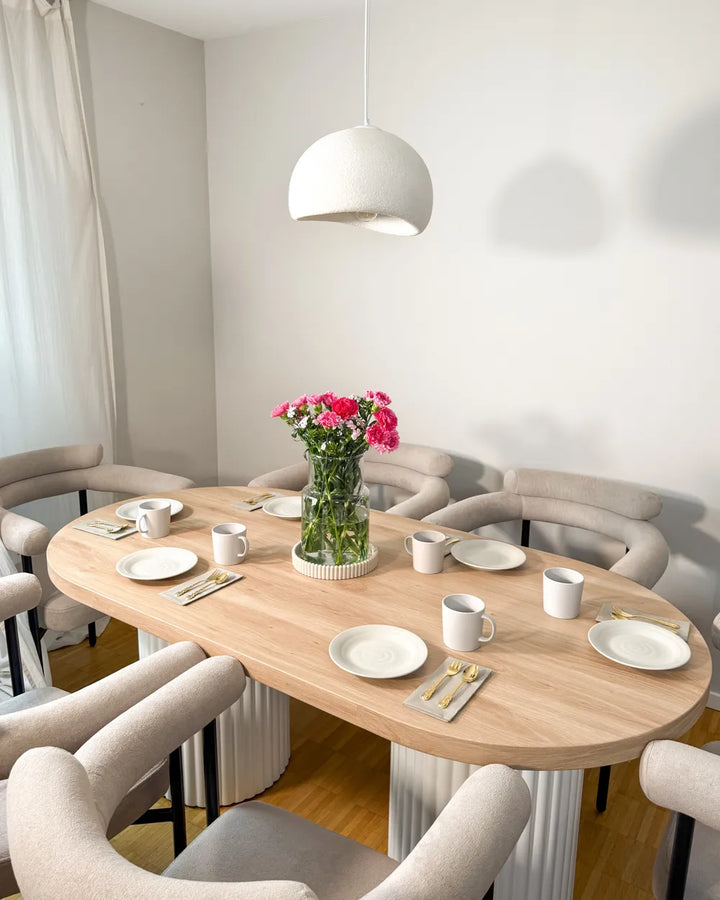 Dining room with a round wooden table set for a meal, featuring plates, cups, and a vase with flowers.