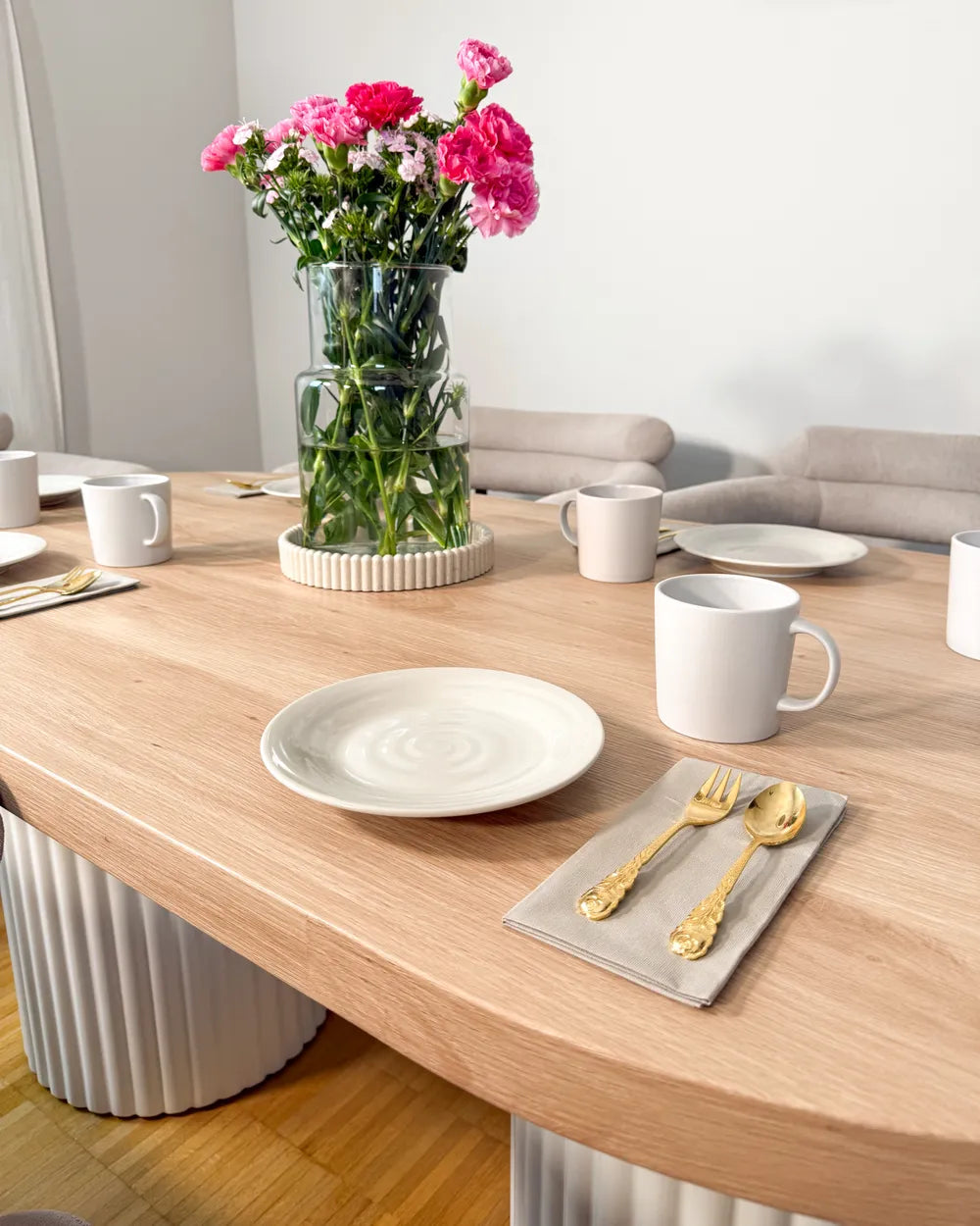 Dining table set with plates, cups, and a vase of flowers in a modern living room.