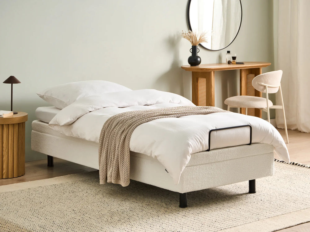 Beige bed in a bedroom setting with wooden side tables and a mirror.
