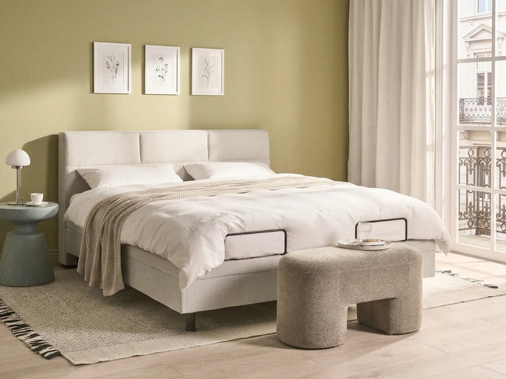 Neatly made bed in a bedroom with a side table and ottoman.
