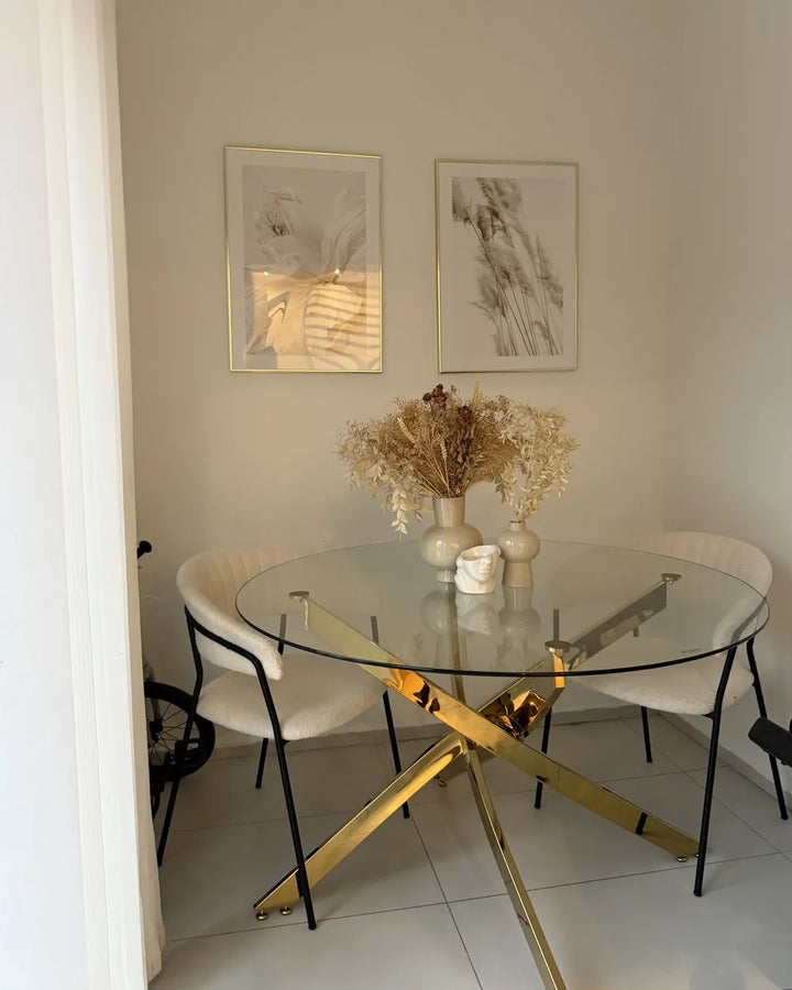 Dining room with a glass table and gold legs, white chairs, and wall art.