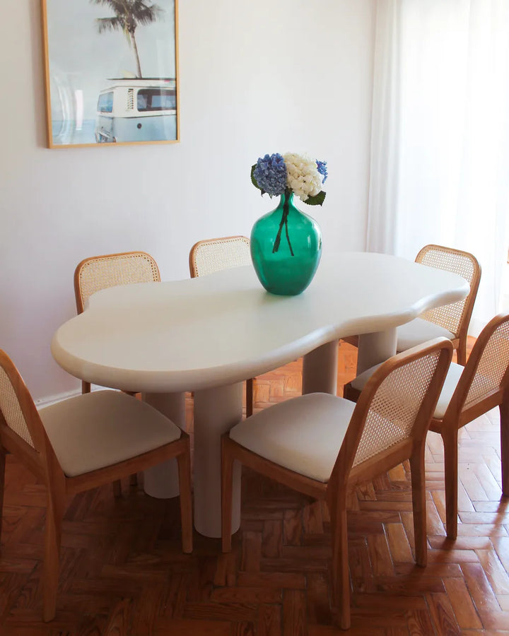 Dining room with a white table and wooden chairs, featuring a green vase with flowers.