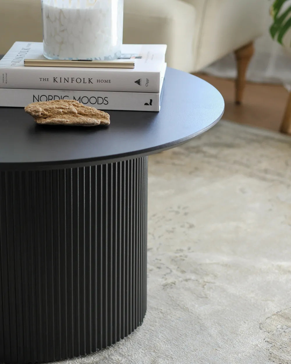 Black cylindrical table with books and a candle on a carpeted floor