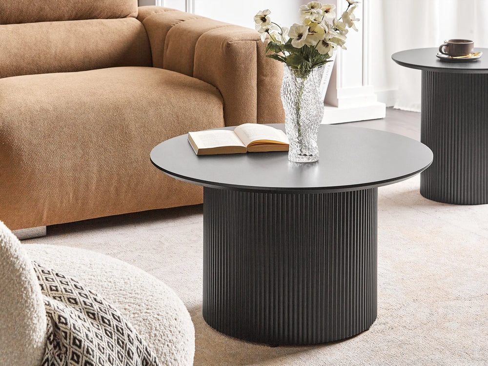 Black coffee table with a vase of flowers and an open book in a living room setting.