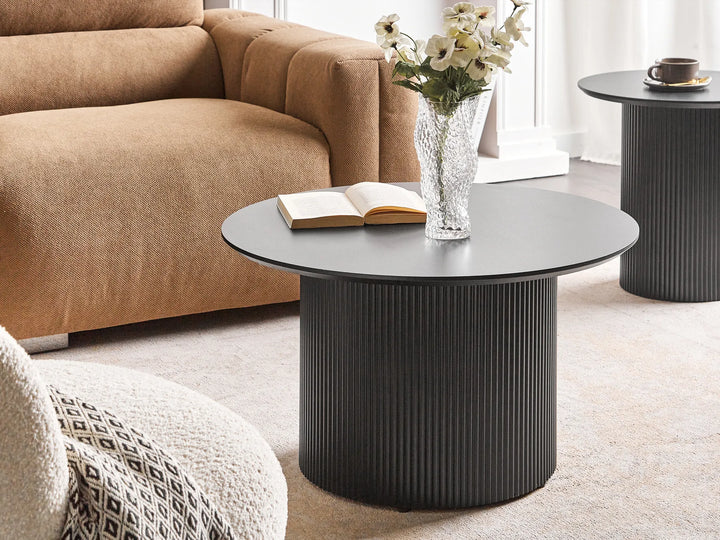 Black coffee table with a vase of flowers and an open book in a living room setting.