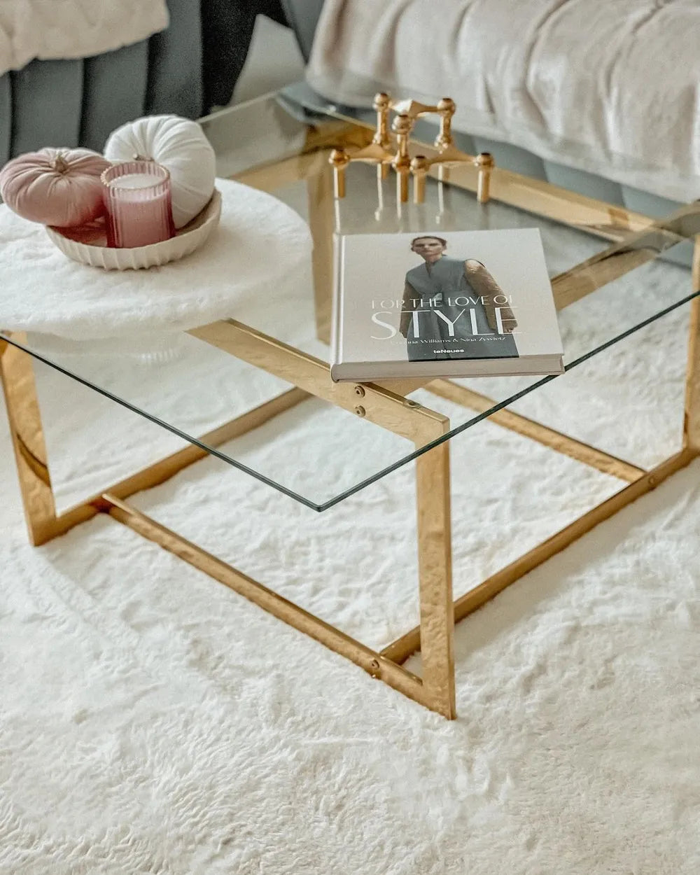 Glass coffee table with gold frame on a white rug, featuring a book titled 'For the Love of Style'.