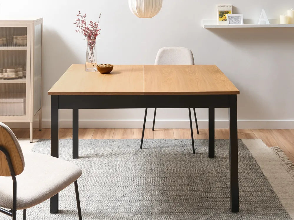 Wooden dining table with black legs in a room setting with chairs and decor.