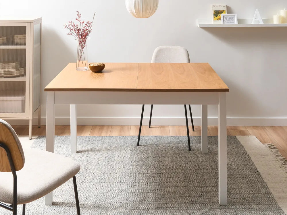 Wooden dining table with white base in a room with shelves and decor.