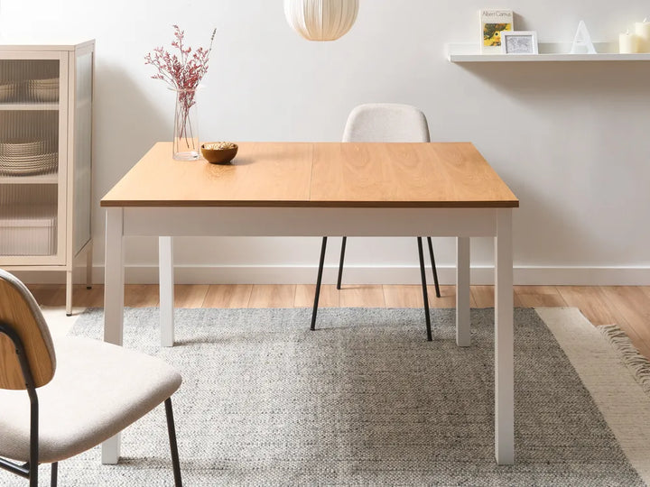 Wooden dining table with white base in a room with shelves and decor.
