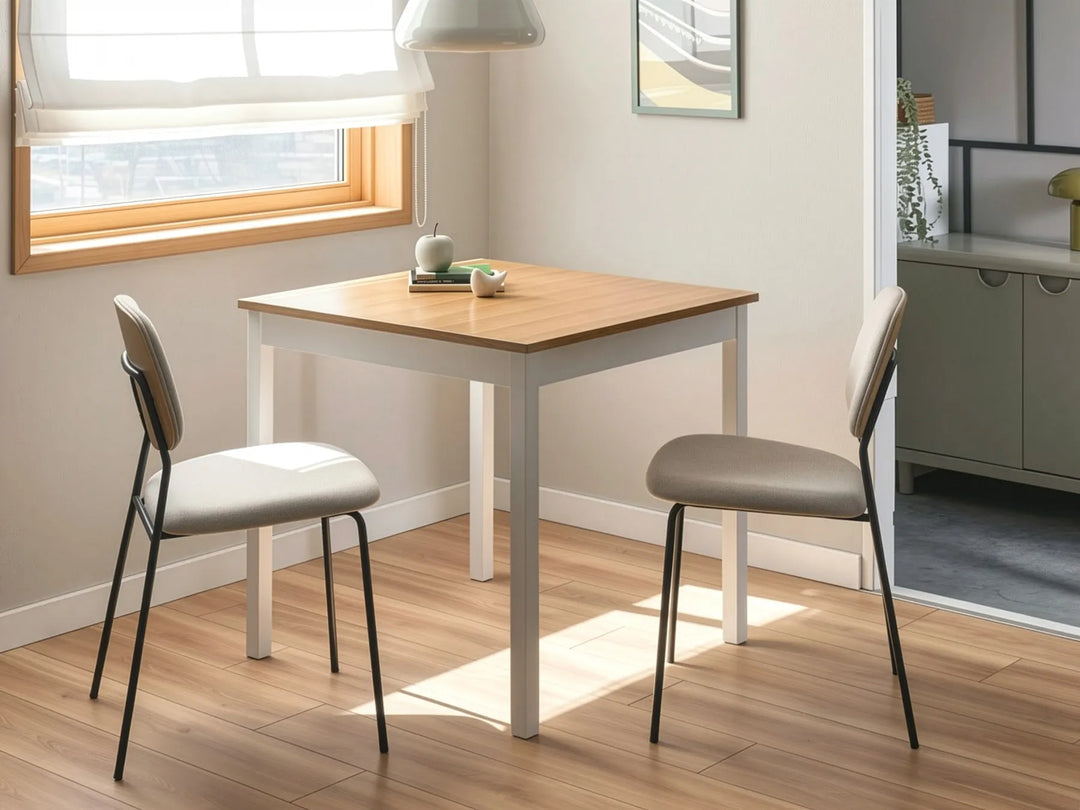 Small dining table with two chairs in a room with a window and a kitchen area.