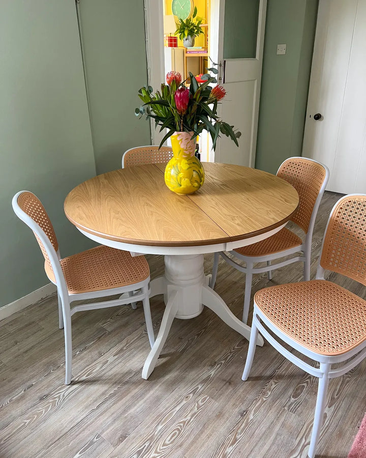 Round wooden dining table with four chairs in a room with light green walls.