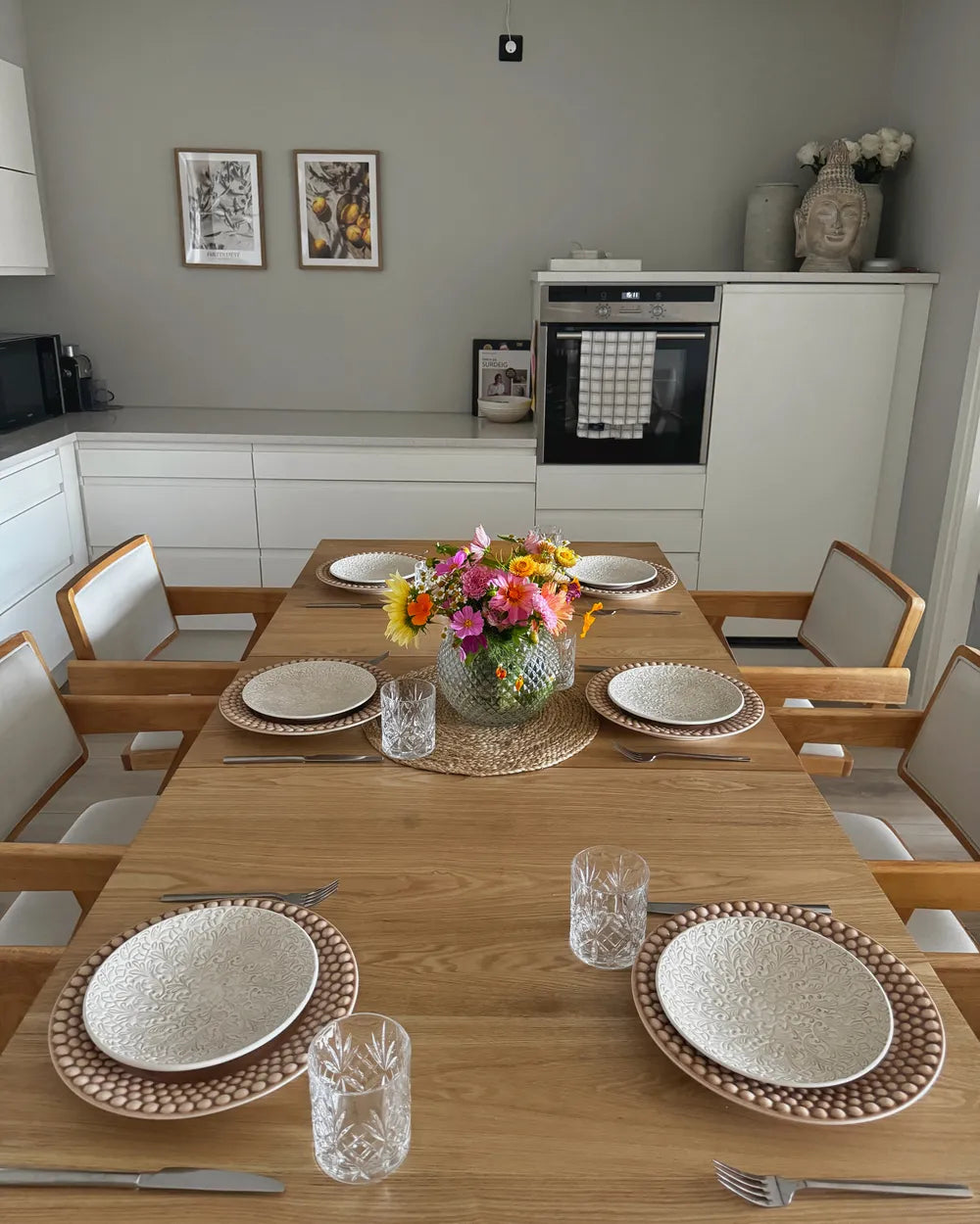 Dining table set with plates, glasses, and a floral centerpiece in a modern kitchen.