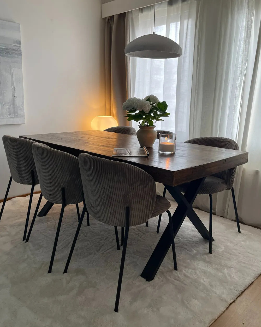 Dining room with wooden table and chairs, light streaming through curtains.