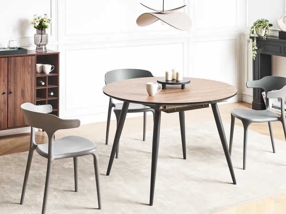 Round wooden dining table with black legs in a modern kitchen setting.