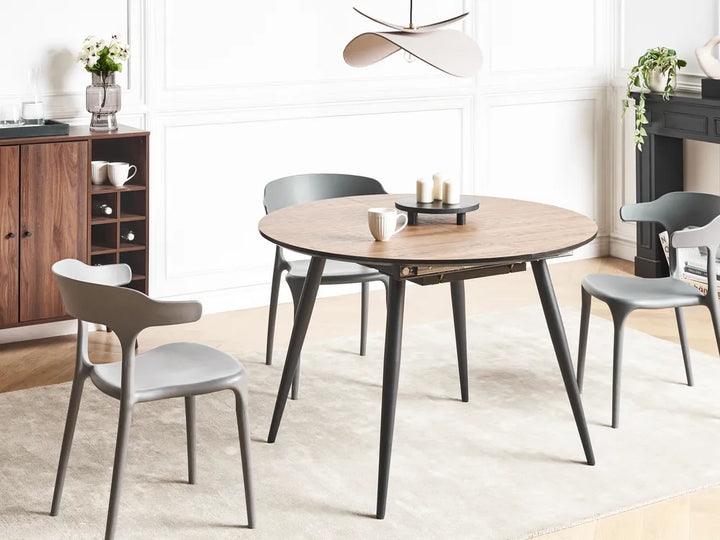 Round wooden dining table with black legs in a modern kitchen setting.