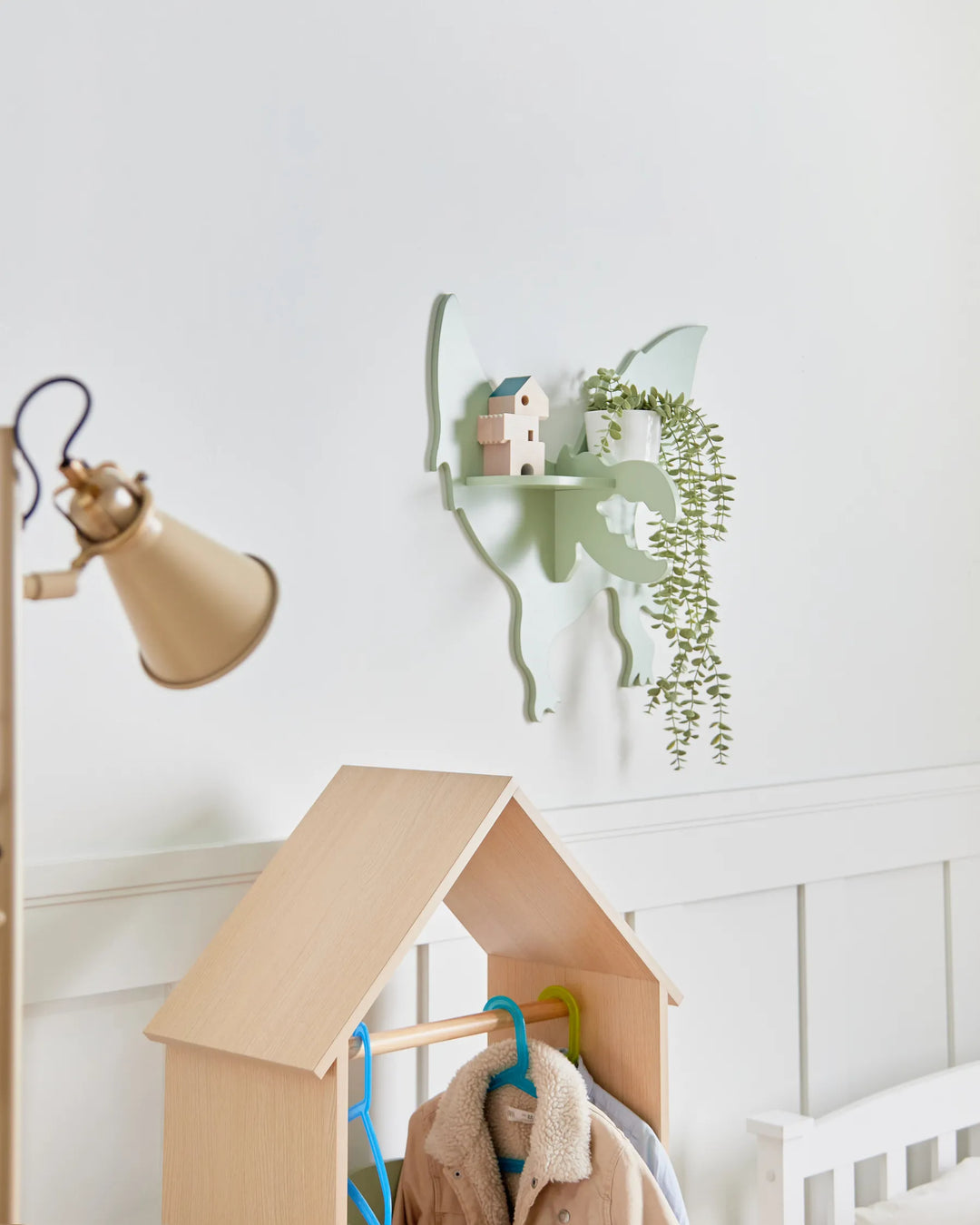 Children's playhouse with coat rack against a white wall with plants and lamp.