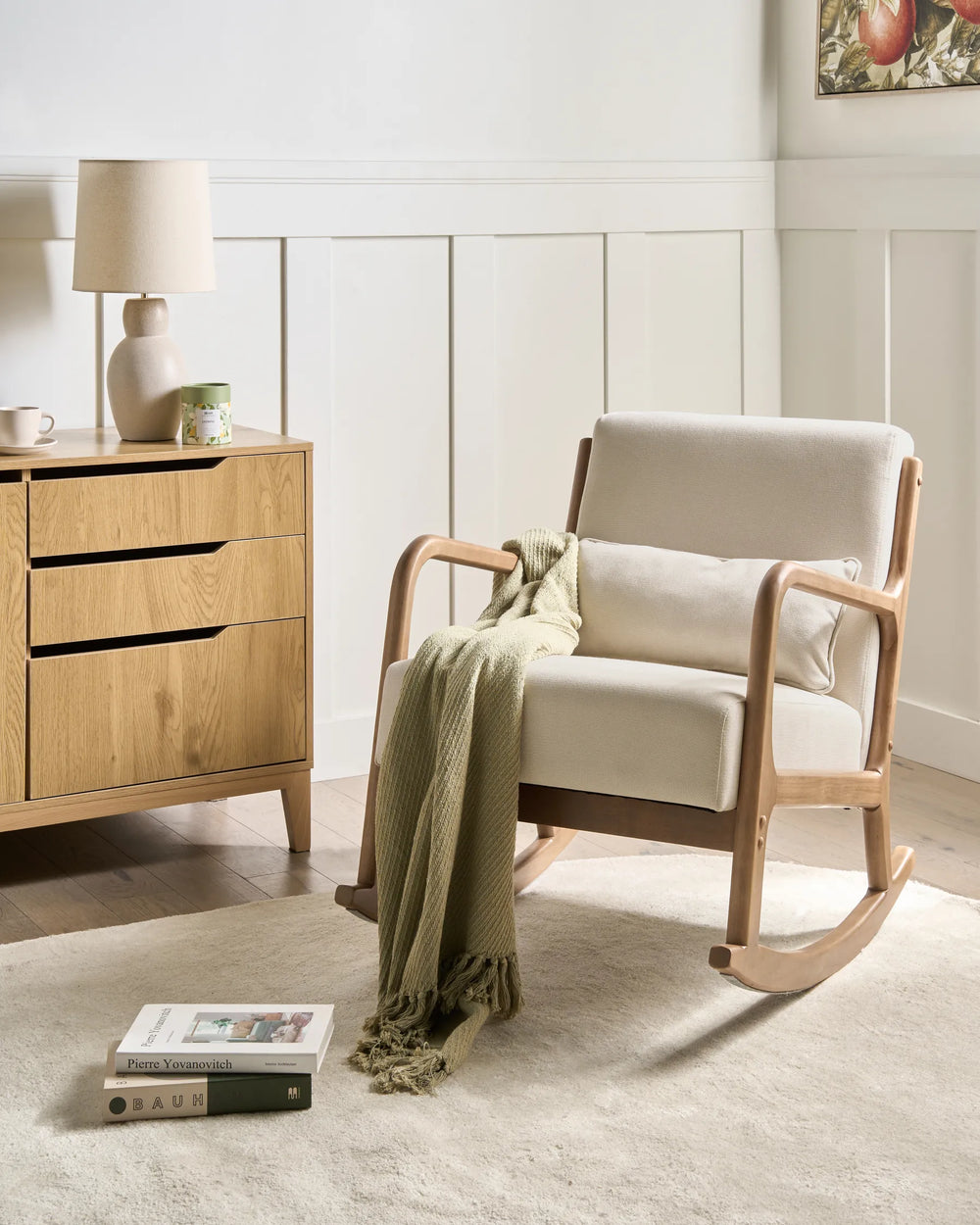 Rocking chair with a green blanket in a room with wooden furniture and a lamp.