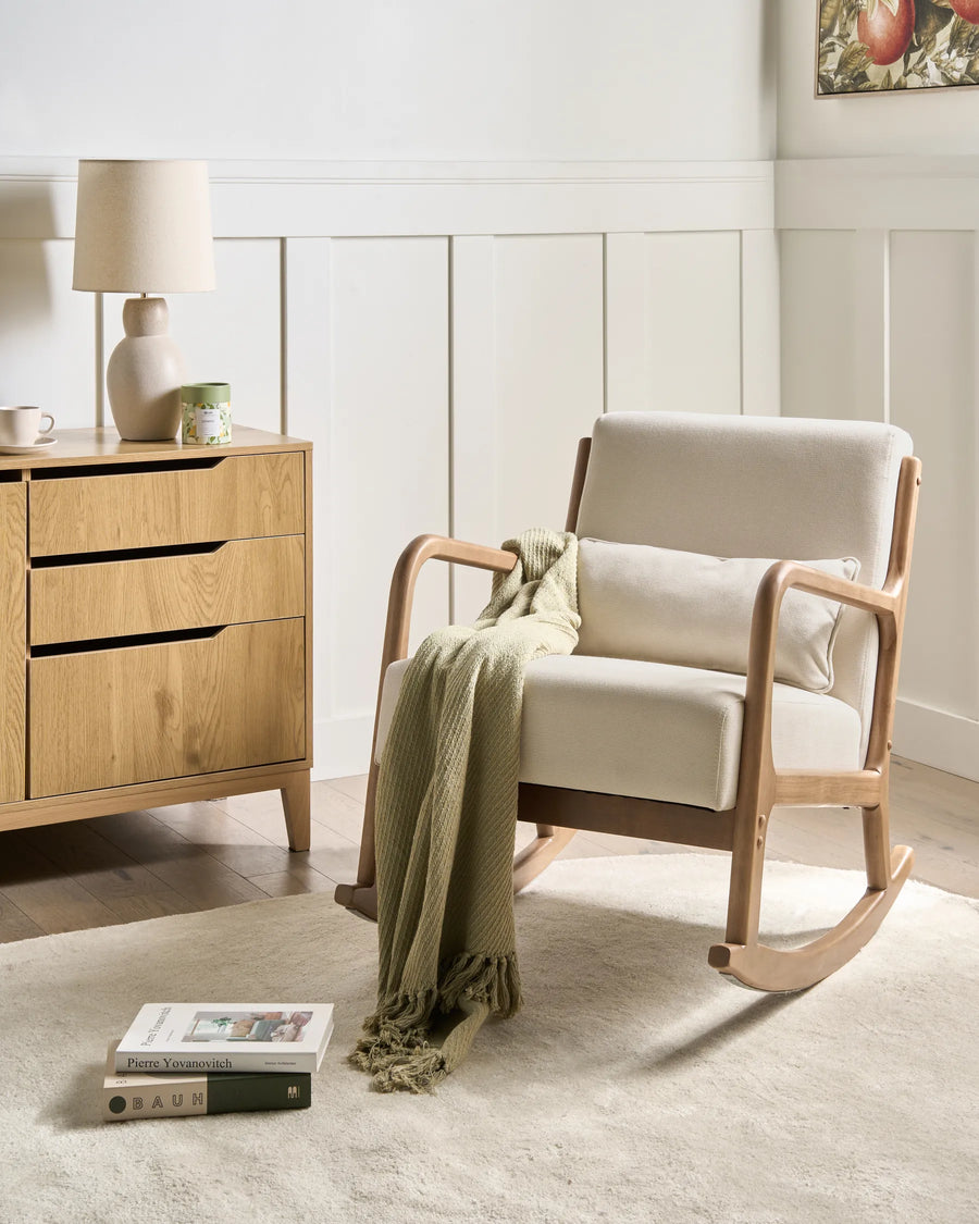 Rocking chair with a green blanket in a room with wooden furniture and a lamp.