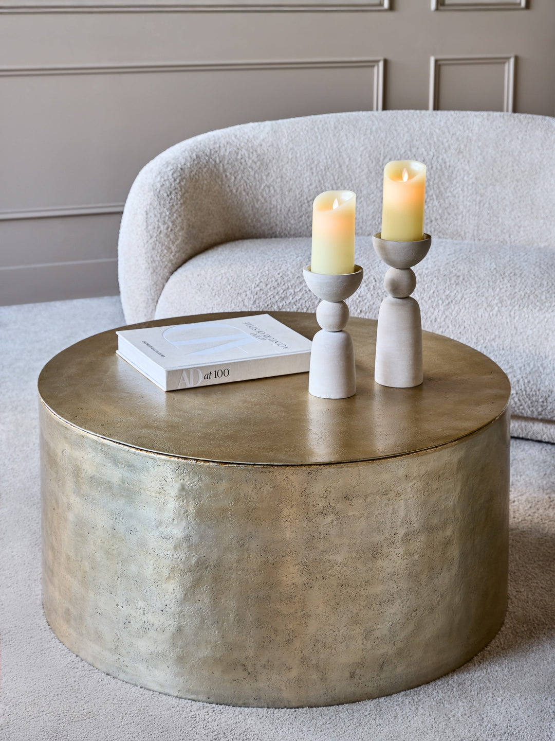 Round metallic coffee table with candles and a book on a neutral background