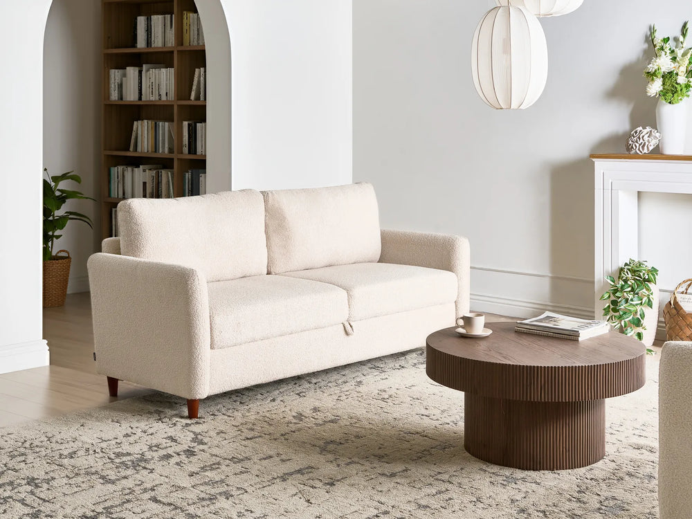 Beige sofa in a living room with a round wooden coffee table and decorative items.