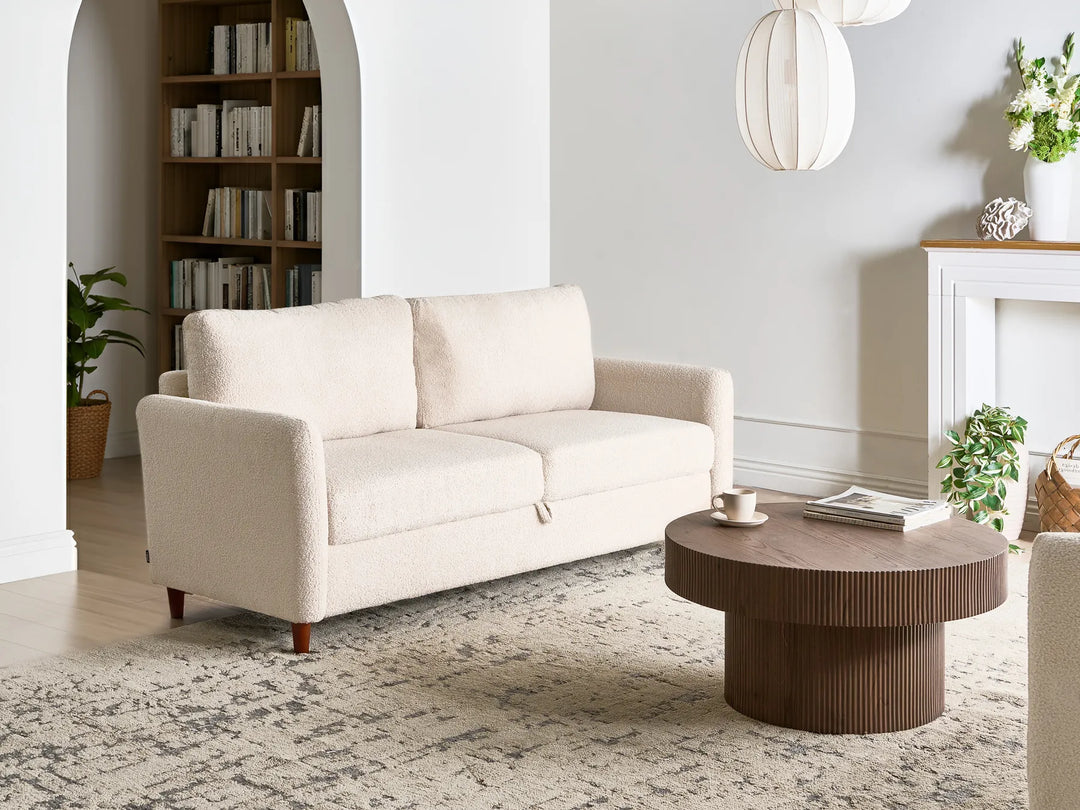Beige sofa in a living room with a round wooden coffee table and decorative items.