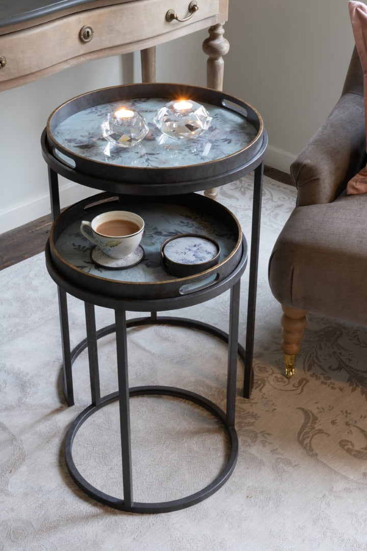 Round metal side table with a cup of coffee and decorative items on a carpeted floor.