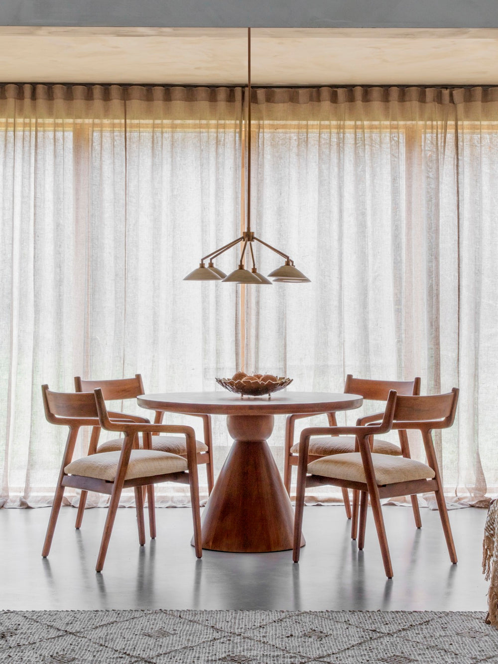 Round dark wood dining table with cone-shaped pedestal in a dining room setting
