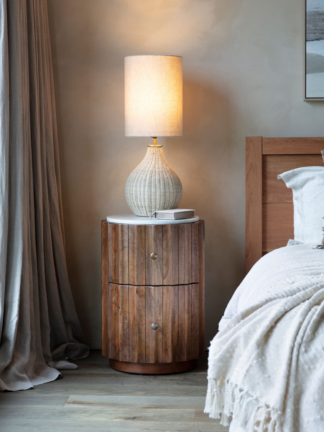 Wooden nightstand with a lamp next to a bed in a bedroom setting