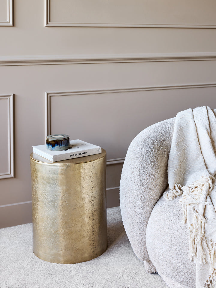 Gold side table with a white chair and decorative items against a beige wall.