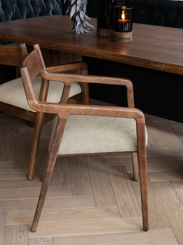 Wooden chair with armrests in a room with wooden flooring and a table.