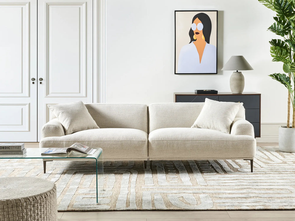 Modern living room with a beige sofa, glass coffee table, and decorative elements.