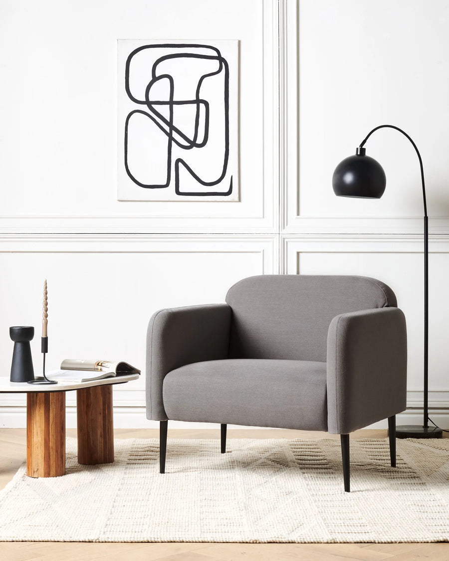 Modern living room with a gray armchair, wooden coffee table, and abstract wall art.