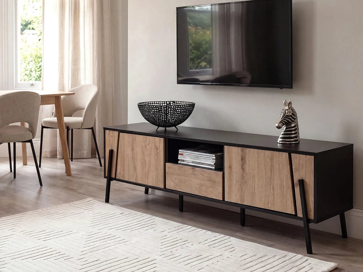 A modern media console with light oak wood doors and a black top, styled in a living room setting with a television mounted on the wall above it.