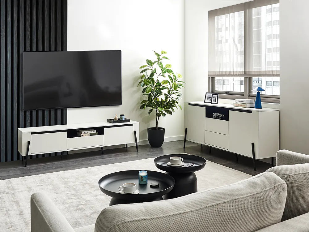 A modern living room setup featuring a white and black media console with a large black TV, a matching white sideboard with a plant, and a light beige sofa in the foreground.