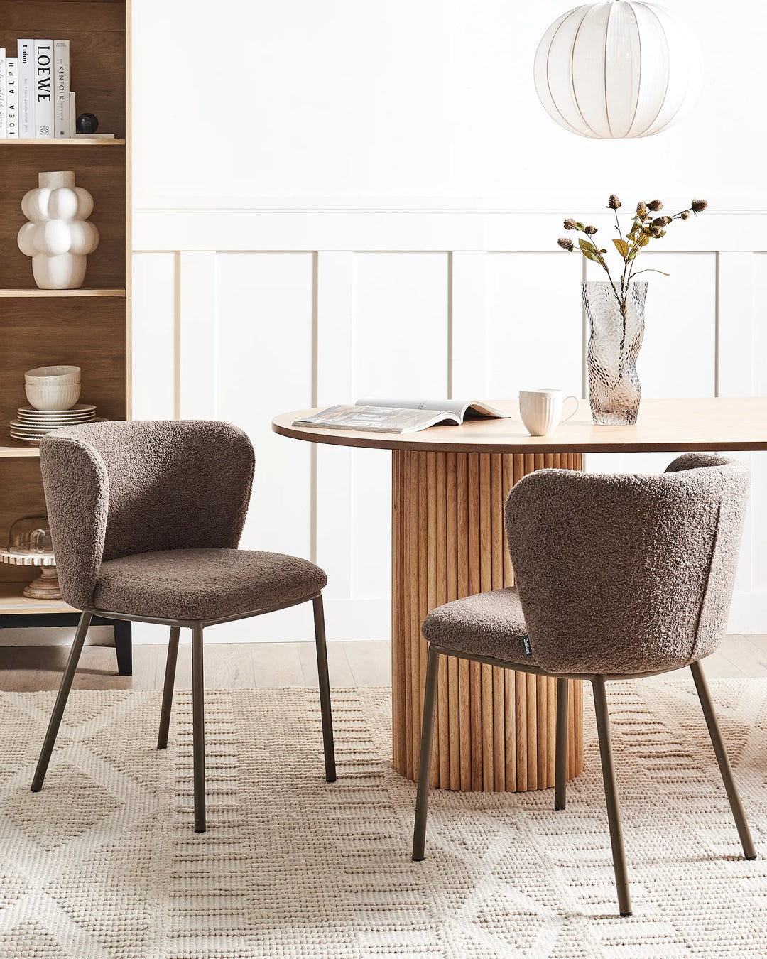 Dining room with two brown chairs around a wooden table, bookshelf in the background.