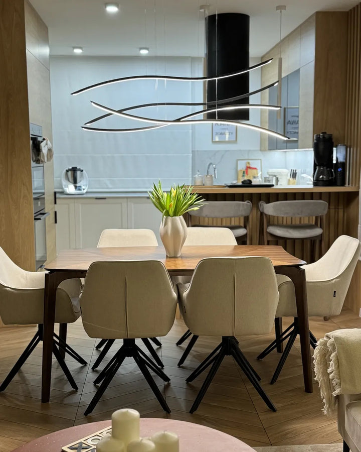 Modern dining room with a wooden table and chairs, kitchen in the background.