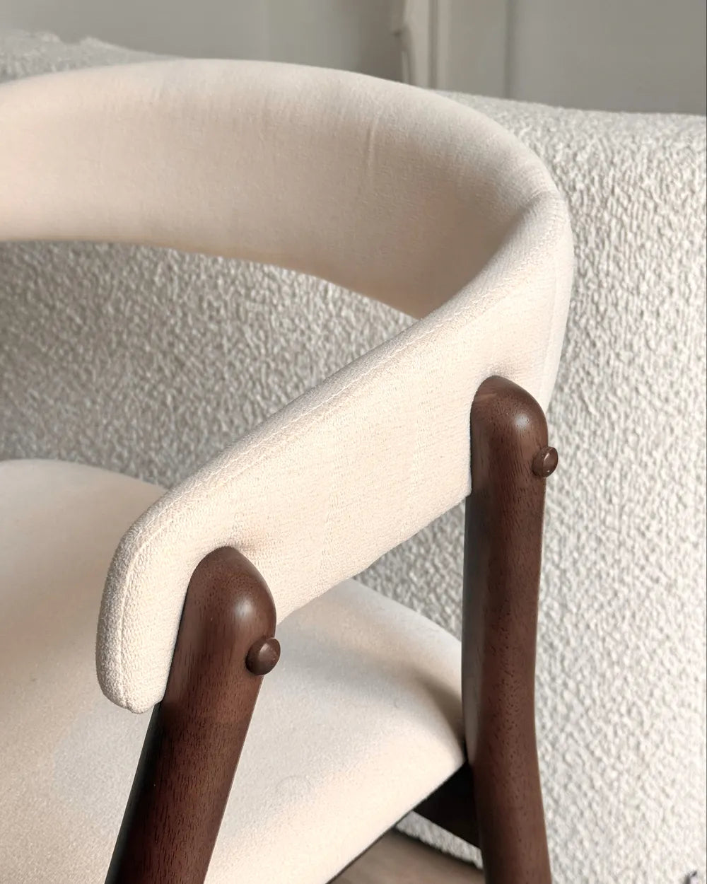 Close-up of a chair with beige cushioned backrest and wooden armrests on a textured surface.