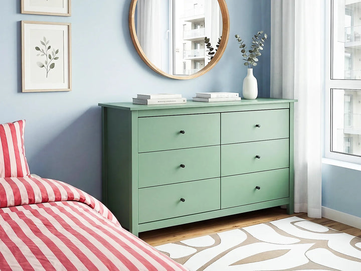 A mint green six-drawer dresser in a styled bedroom setting with a light blue wall, a red and white striped bed, a round mirror, and a window.