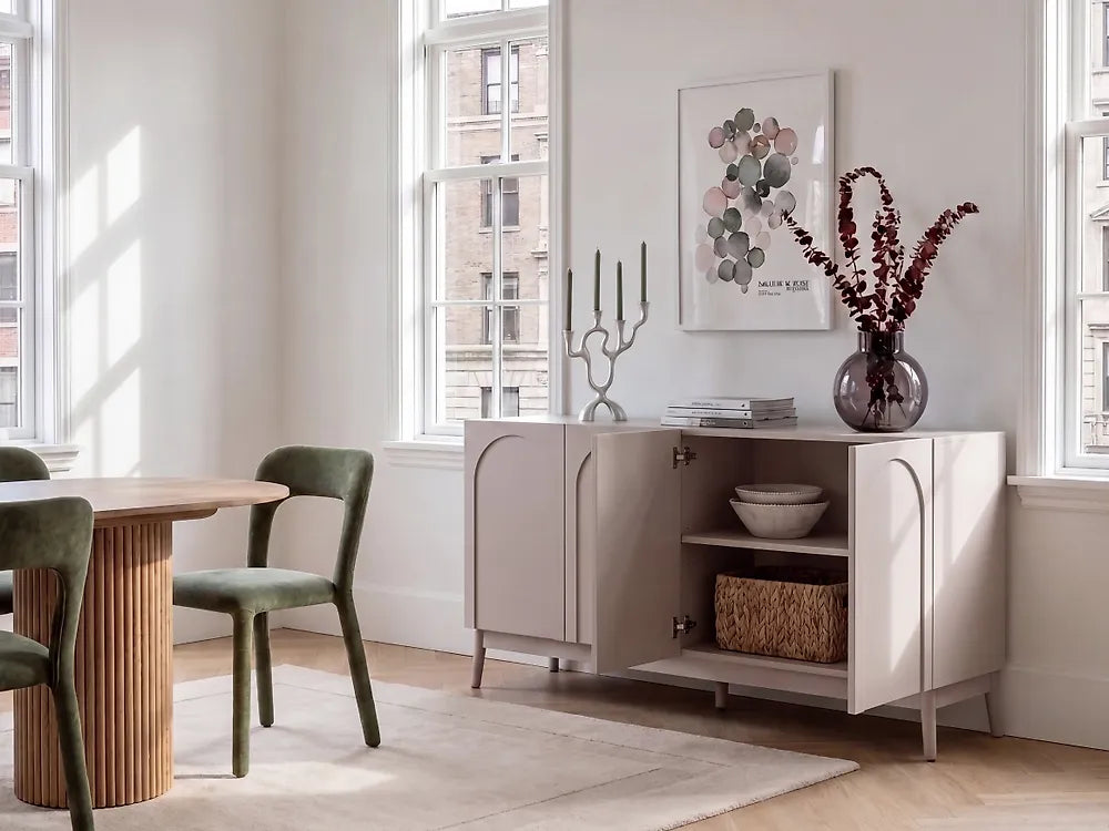 A light beige sideboard cabinet in a bright, modern dining room setting with green chairs, a wooden table, and decorative items on top.