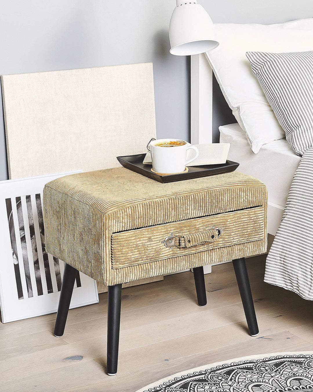 Beige textured nightstand with a drawer next to a bed with striped bedding.