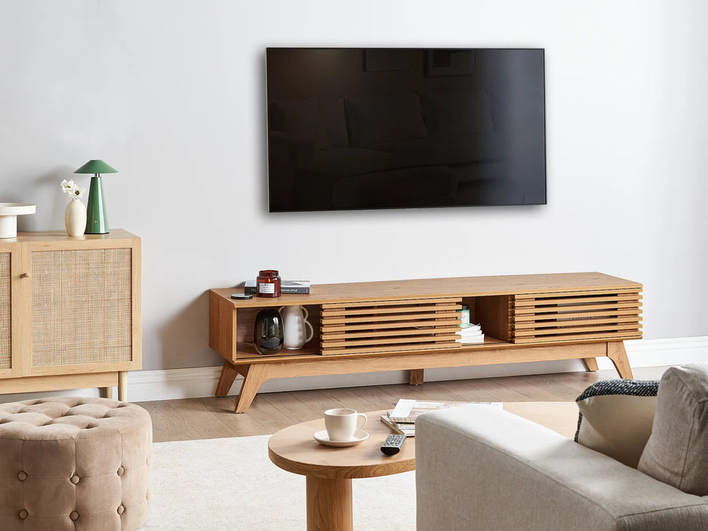 A modern wooden TV stand console with slatted front panels and open shelving, shown in a styled living room setting below a wall-mounted television.