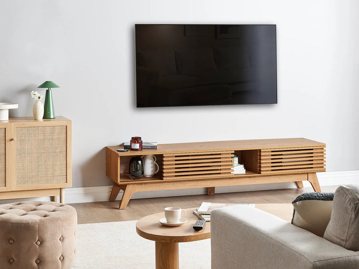A modern wooden TV stand console with slatted front panels and open shelving, shown in a styled living room setting below a wall-mounted television.