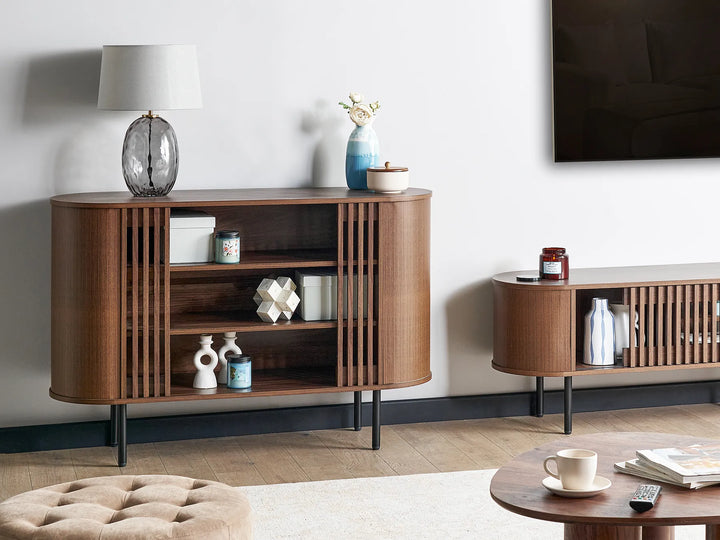 A mid-century modern wooden sideboard cabinet with curved fronts, vertical slat details, and open shelves, styled in a living room setting next to a matching TV console.