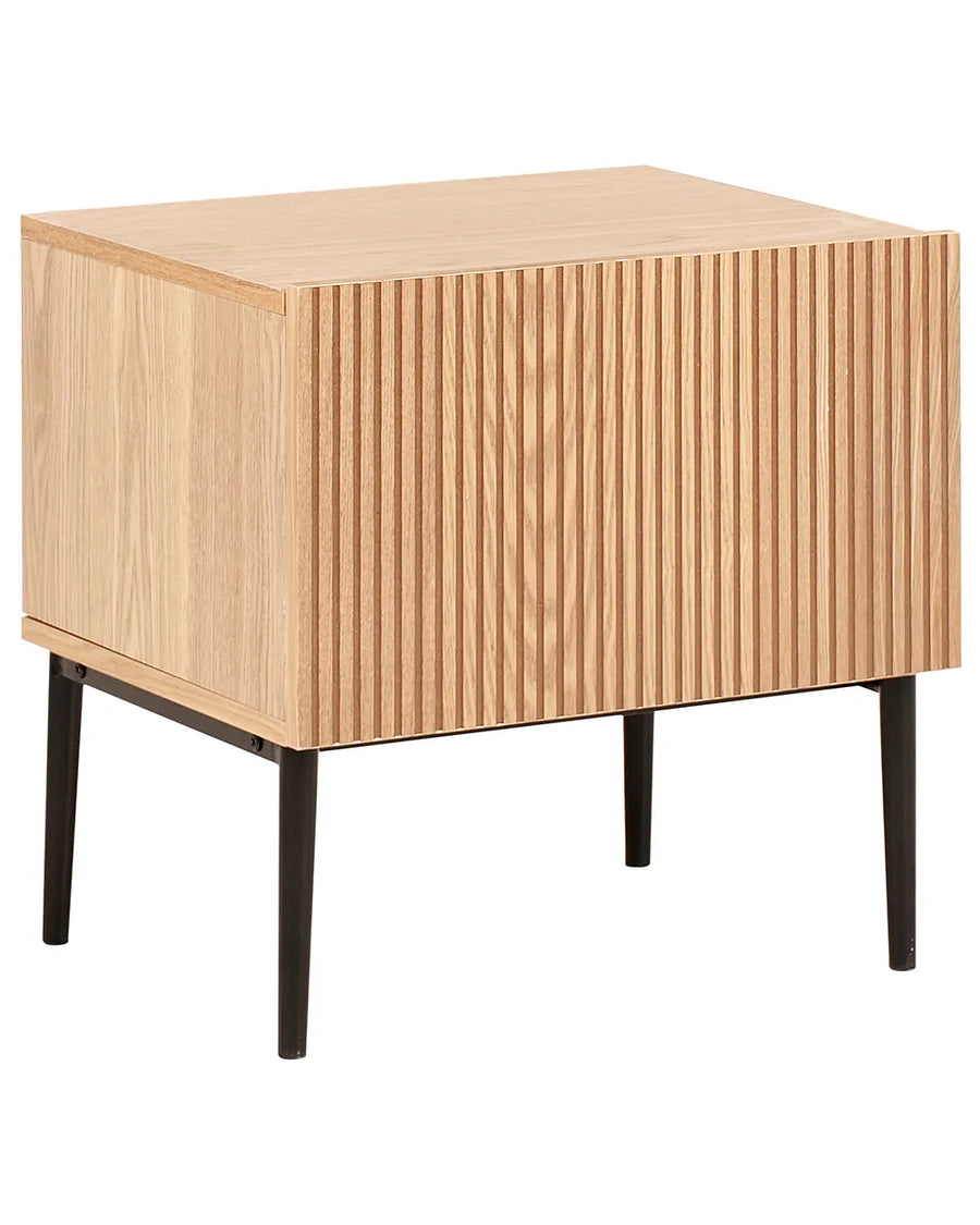 A modern wooden side table with a light natural oak finish, featuring vertical fluted slats on the front and back panels and four tapered black metal legs, shown against a plain white background.