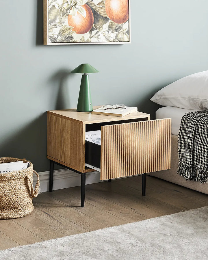 Wooden nightstand with a lamp next to a bed in a bedroom setting.