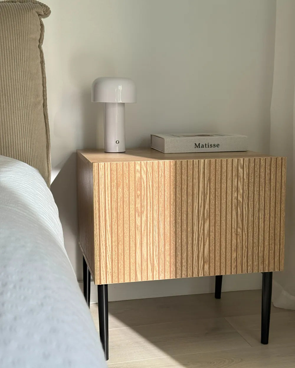 Wooden nightstand with a lamp and book next to a bed
