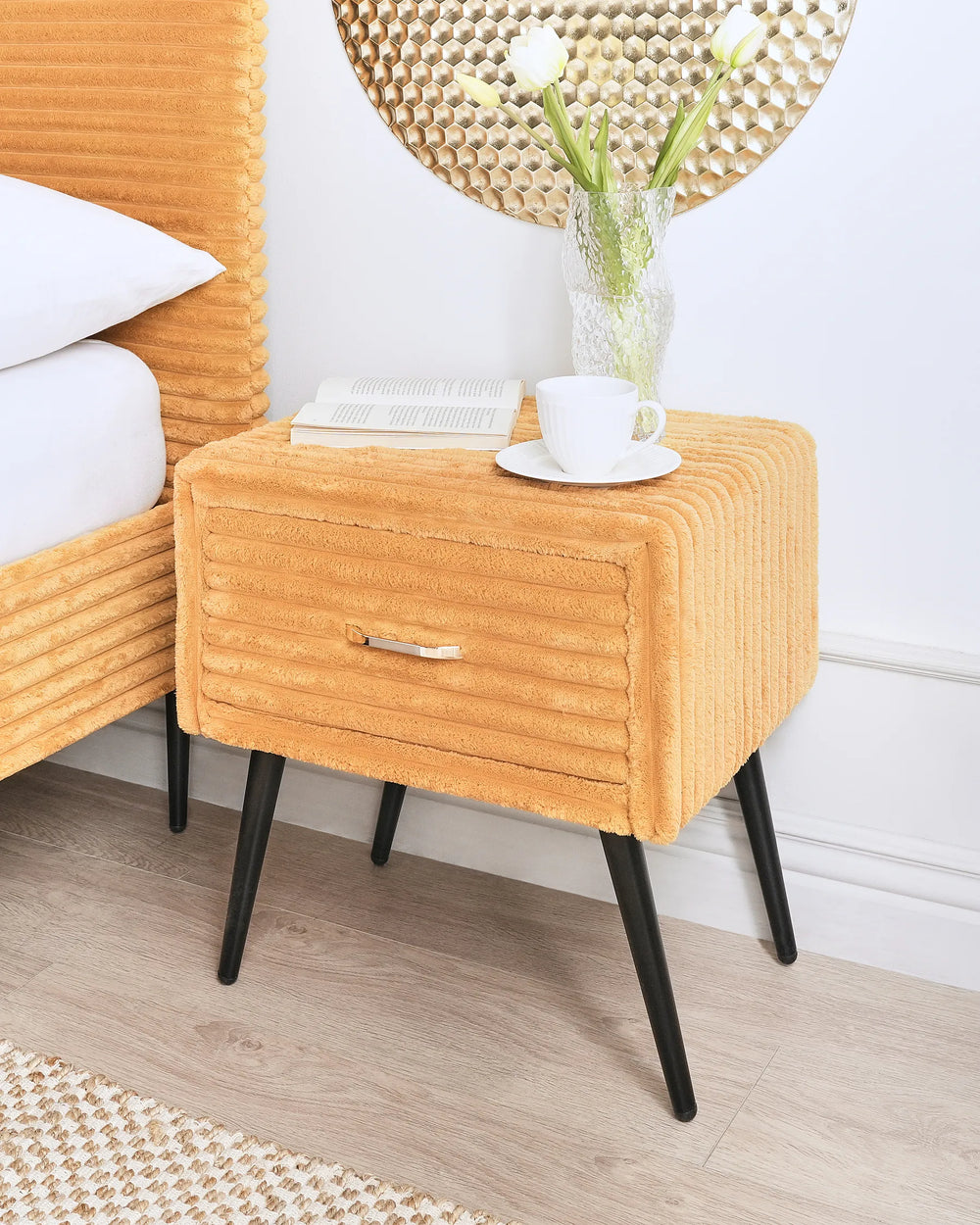 Orange nightstand with a drawer, cup, and saucer in a bedroom setting.