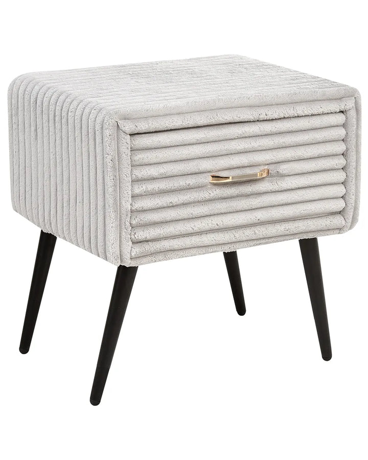 A square upholstered side table or nightstand with a ribbed light gray fabric, black tapered legs, and a small metallic gold drawer pull, shown on a plain white background.