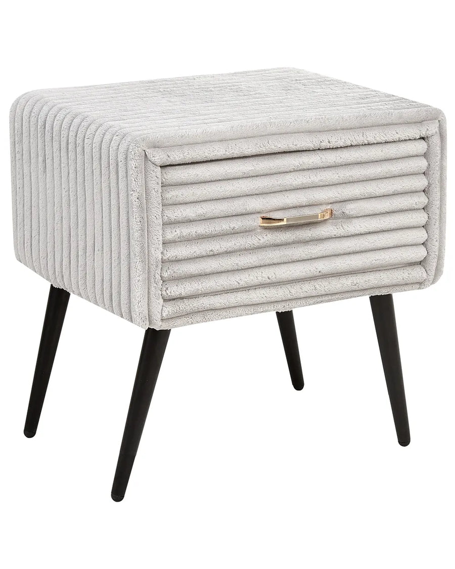 A square upholstered side table or nightstand with a ribbed light gray fabric, black tapered legs, and a small metallic gold drawer pull, shown on a plain white background.