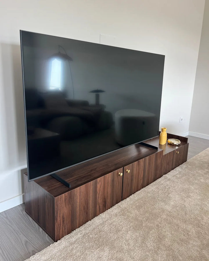 A large flat-screen television mounted above a dark wood media console in a home interior with light walls and a beige carpet.